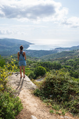 Young woman admiring panorama from hill overseeing bay in Tuscany wearing denim dungaree