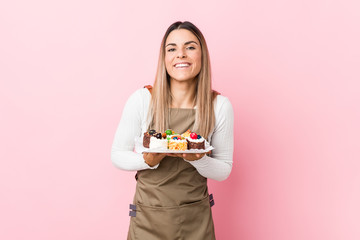 Young baker woman holding sweets laughing and having fun.
