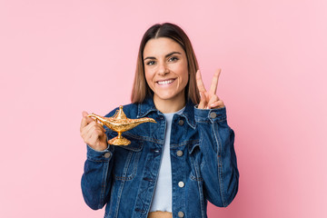 Young caucasian woman holding a magic lamp showing victory sign and smiling broadly.