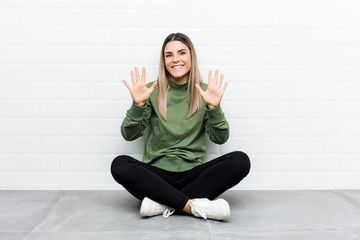 Young caucasian woman sitting on the floor showing number ten with hands.