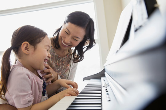 Mother teaching daughter to play piano
