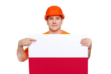 smiling middle-aged worker wearing orange hard hat, holding sheet with polish flag in hands
