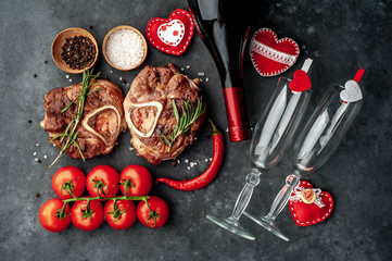 two grilled steaks, with tomatoes and spices with a bottle of wine and glasses, various red hearts on a stone background. dinner for two on valentine's day