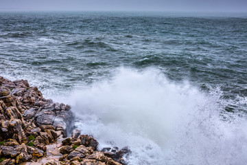 A huge ocean waves breaking on the coastal cliffs in at the cloudy stormy day. Breathtaking romantic seascape of ocean coastline.