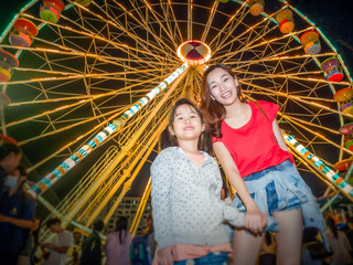 Obraz na płótnie Canvas happy asia mother and daughter have fun in amusement carnival park with farris wheel and carousel background
