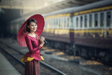 Traveler Asia girl wear traditional dress with umbrella waits for train on railway platform,...