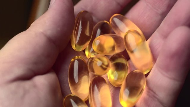 Man pours Omega 3 vitamin gel capsules into hand from pill bottle, close-up