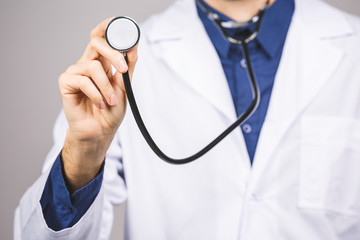 Handsome young medic doctor holding a stethoscope, isolated over grey background.