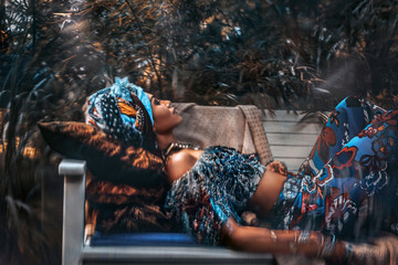 Fototapeta na wymiar beautiful young stylish woman wearing turban lying on the bench in garden on tropical background