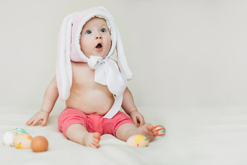 small beautiful baby sitter in rabbit hat. girl celebrates Easter and found painted eggs.