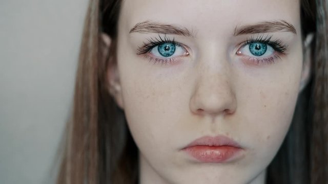 Young teenager girl opens her beautiful blue eyes and looks at the camera, close-up in a slow motion
