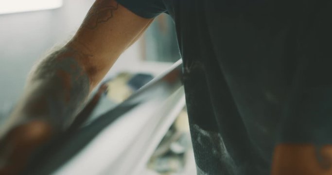 Surfboard shaper carefully shaping a surfboard rail with his hands and sandpaper, surfboard craftsman concept