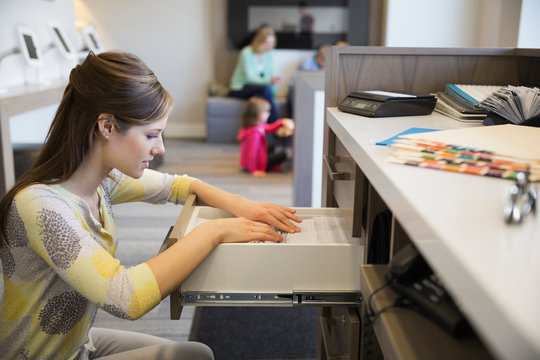 Receptionist Looking Through Drawer In Dentists Office