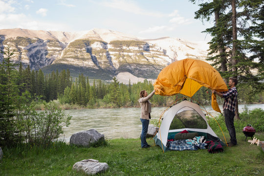 Couple assembling tent at campsite near mountains