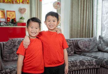 two kids smile in red shirts standing at front a couch