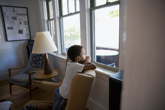 Boy with headphones looking out living room window