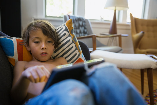 Boy using digital tablet on living room sofa