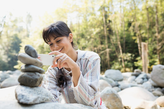Young woman photographing stacked stones in woods