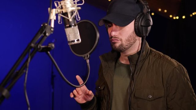 4K: Male Singer / Popstar recording an Album in the studio - He sings into the Microphone with headphones & Baseball Cap on