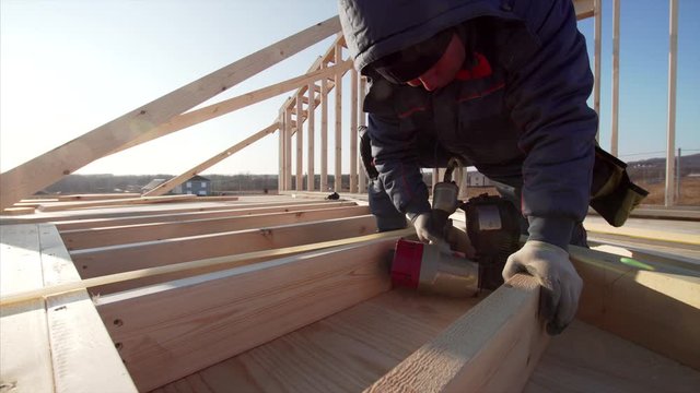Builder in gloves is adjusting wooden planks with manual and hydraulic hammer at frame house building at sunny day