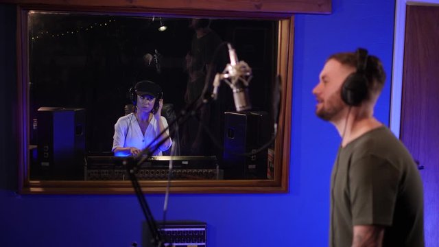 Male Singer / Popstar recording Album in the studio - With female Sound Engineer in front mixing the track