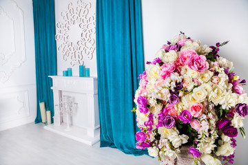 Beautiful interior in blue with a huge vase with bright and colorful flowers, with a decorative fireplace and blue curtains, with blue candles on the fireplace and stucco on the wall