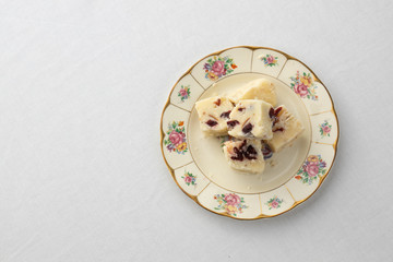 White fudge with cranberries on a pretty floral plate on a white tablecloth