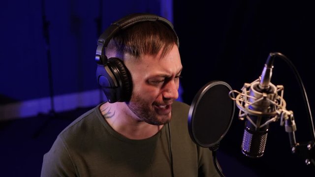 Male Singer / Popstar recording an Album in the studio - He sings into the Microphone wearing headphones 
