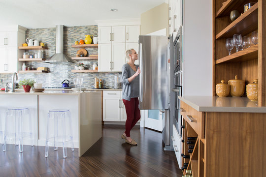 Woman Opening Refrigerator Door In Kitchen