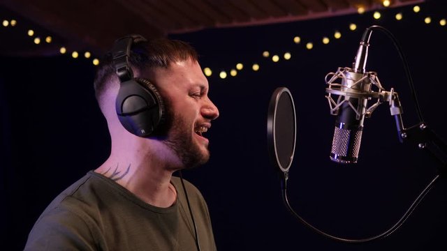Male Singer / Popstar recording an Album in the studio - He sings into the Microphone with headphones on. Tilt Up