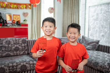 two kids smile in red shirts with angpau standing at front a couch