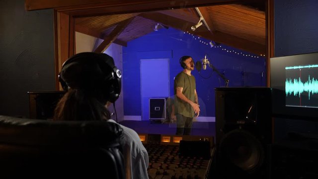Male Singer / Popstar recording an Album in the studio in background - With female Sound Engineer in front mixing the track