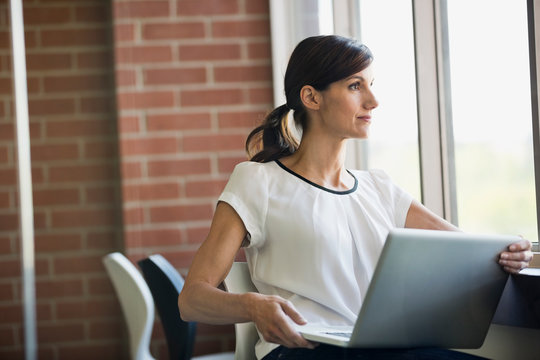 Businesswoman with laptop looking out window in office