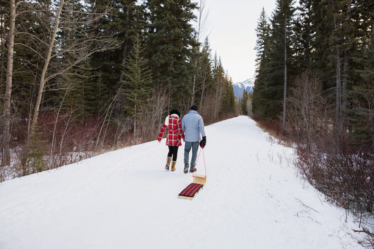 Couple pulling sled down snowy lane in woods