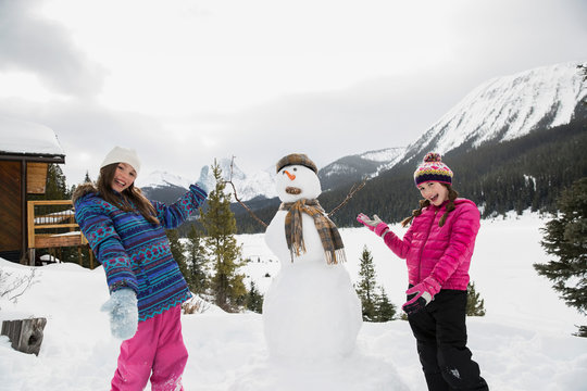Portrait of proud girls with snowman below mountains
