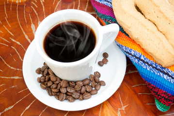  Cup of coffee accompanied by toast or cookie called Herraje, typical tablecloth on wooden table.