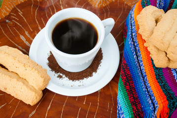  Cup of coffee accompanied by toast or cookie called Herraje, typical tablecloth on wooden table.