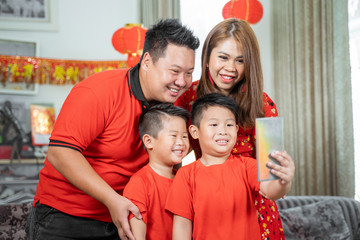 Obraz na płótnie Canvas Asian family with two son smiling holding cell phone to take selfie with father and mother.Asian Chinese family celebrates Lunar New Year