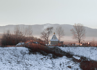 A small monastery building on a frosty winter morning on a background of hills covered with foggy haze