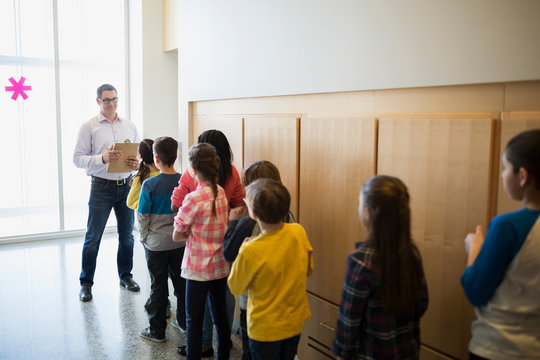 Teacher with clipboard and students lined up corridor