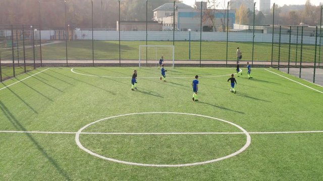 Aerial view of little footballers training outdoors, skillful forward taking pass, bypassing back players and missing while trying to score goal. Kids soccer team playing on green football field
