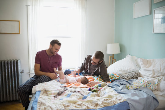 Homosexual couple playing with baby on bed