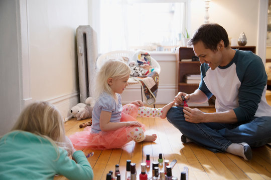 Father painting daughter toenails with fingernail polish