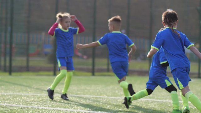 Active group of young soccer players doing warm up exercise while running around football field and playing catch-up with ball. Joyful preadolescent children training outdoors before football match