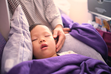 Cute little Asian 3 years old toddler boy child sleeping on airplane, Kid sleeping on mother's laps during the flight by plane, Flying with children concept - Soft & Selective focus