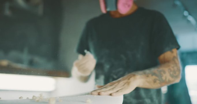 Surfboard shaper using a planer tool to shape a surfboard stringer, skilled craftsman working with his hands shaping a new surfboard