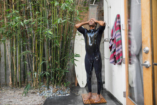 Man in wet suit surfboard using outdoor shower