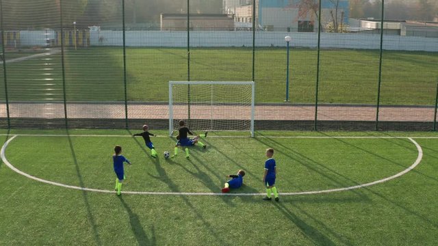 Aerial view of future footballers playing on green football pitch while developing skill of teamwork during match. Drone shot of preadolescent kids running with ball across field and scoring goal