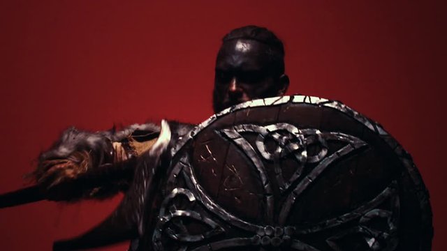 The Viking hits his round shield with an axe. A hostile bandit in warm armor is preparing to attack. Blazing fire in the background