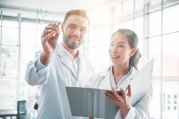 Scientists drawing chemical formulas on clear glass board and colleague are watching